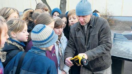 Wärme in der Kälte. Die fünfte Klasse der Pankower Grundschule unter den Bäumen fotografiert mit einer Wärmebildkamera ihre Schule und ihre alte Turnhalle. Jens Clemen erklärt den Schülern, was die roten und gelben Bilder bedeuten. Clemen ist Leiter des Projekts „Köpfchen statt Kohle“, das der Bezirk Pankow ins Leben gerufen hat und das Schulen beim Energiesparen unterstützt. 