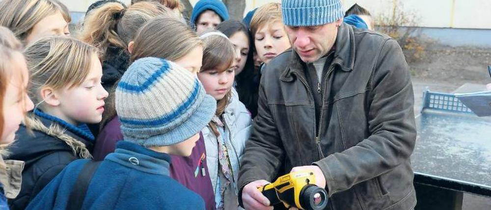 Wärme in der Kälte. Die fünfte Klasse der Pankower Grundschule unter den Bäumen fotografiert mit einer Wärmebildkamera ihre Schule und ihre alte Turnhalle. Jens Clemen erklärt den Schülern, was die roten und gelben Bilder bedeuten. Clemen ist Leiter des Projekts „Köpfchen statt Kohle“, das der Bezirk Pankow ins Leben gerufen hat und das Schulen beim Energiesparen unterstützt.