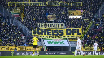 Fußball: Bundesliga, FC Augsburg - Borussia Dortmund, 15. Spieltag, WWK-Arena. Fans von Borussia Dortmund halten ein Plakat mit der Aufschrift „Wir werden kein Teil eures Deals sein! Scheiss DFL“ in die Luft. Das Fan-Bündnis «Unsere Kurve» fordert eine Wiederholung der Abstimmung beim Investoren-Deal. (zu dpa: «Investoren-Deal: Fan-Bündnis fordert Wiederholung der Abstimmung») +++ dpa-Bildfunk +++