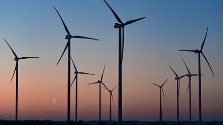 Farbenprächtig leuchtet der Morgenhimmel und die Mondsichel kurz vor Sonnenaufgang hinter Windenergieanlagen. (Symbolfoto)