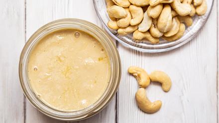 A jar of cashew butter with a bunch of fresh cashew on a white wooden table. Homemade cashew butter, natural, healthy food. The modern wellness and vegan concept.