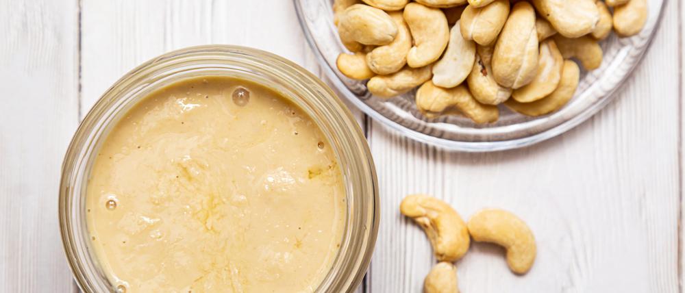 A jar of cashew butter with a bunch of fresh cashew on a white wooden table. Homemade cashew butter, natural, healthy food. The modern wellness and vegan concept.