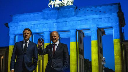 Kanzler Olaf Scholz and Frankreichs Präsident Emmanuel Macron (l.) am Brandenburger Tor, das in den Farben der Ukraine angestrahlt ist. 