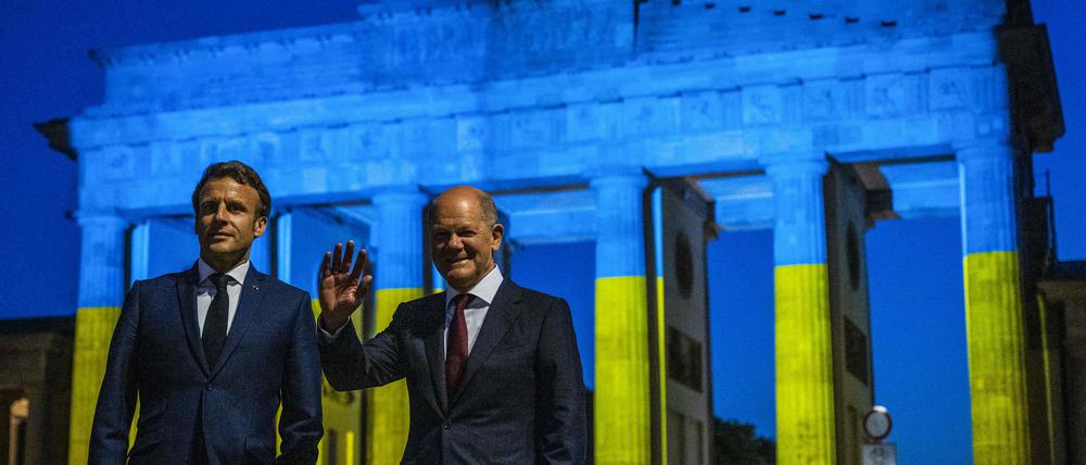 Kanzler Olaf Scholz and Frankreichs Präsident Emmanuel Macron (l.) am Brandenburger Tor, das in den Farben der Ukraine angestrahlt ist. 