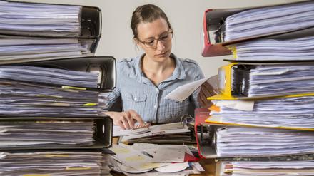 Frau arbeitet am Schreibtisch zwischen Aktenbergen.  