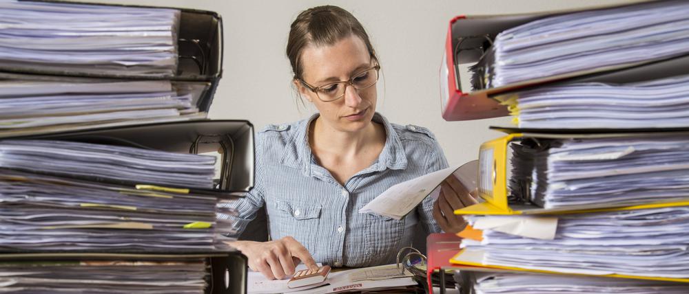 Frau arbeitet am Schreibtisch zwischen Aktenbergen.  