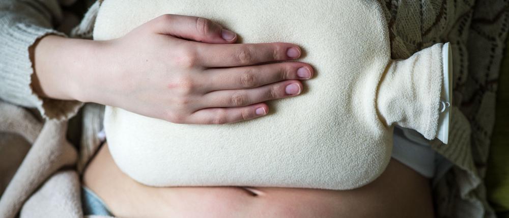 Eine junge Frau hält sich wegen Bauchschmerzen eine Wärmflasche.