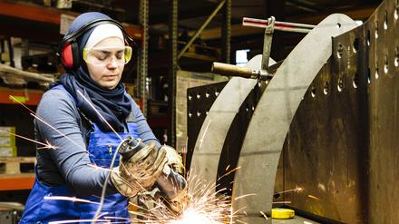 Young female trainee welds steel with grinder in workshop, flying sparks