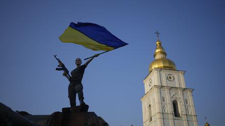 Eine Frau schwenkt die ukrainische Flagge auf einem zerstörten russischen Panzer. 