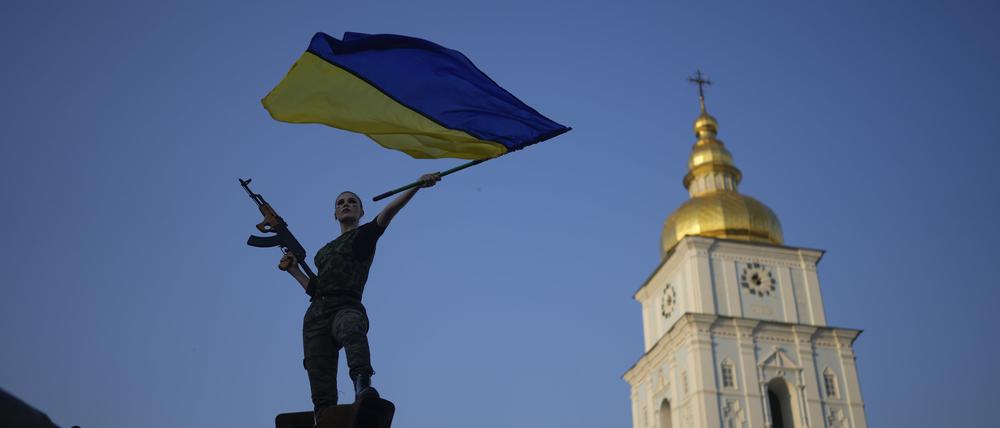 Eine Frau schwenkt die ukrainische Flagge auf einem zerstörten russischen Panzer.