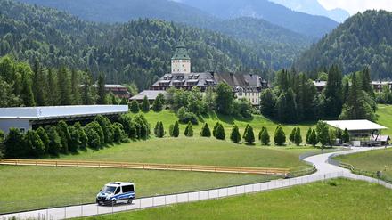 Ein Polizeiauto fährt die Straße von Schloss Elmau herunter, links ist der Pressebereich und rechts die Pressetribüne zu sehen. 