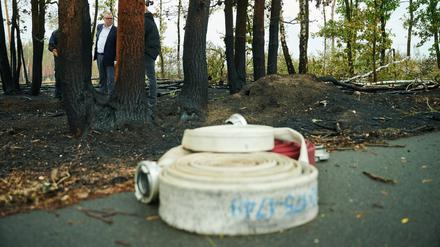 Schläuche der Feuerwehr liegen auf dem Boden, während Michael Stübgen (CDU), Innenminister des Landes Brandenburg im verbrannten Wald in Treuenbrietzen steht. 