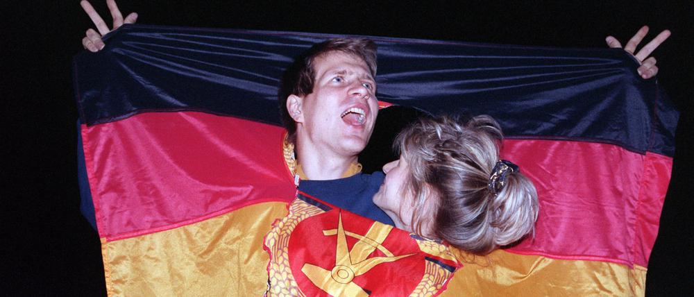 Ein jubelnden Paar hat sich am 3. Oktober 1990 in einer DDR-Fahne dort Platz geschaffen, wo früher das Emblem Hammer und Sichel war - und feierte frenetisch den historischen Anlass.