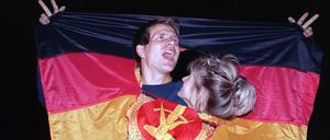 Ein jubelnden Paar hat sich am 3. Oktober 1990 in einer DDR-Fahne dort Platz geschaffen, wo früher das Emblem Hammer und Sichel war - und feierte frenetisch den historischen Anlass.