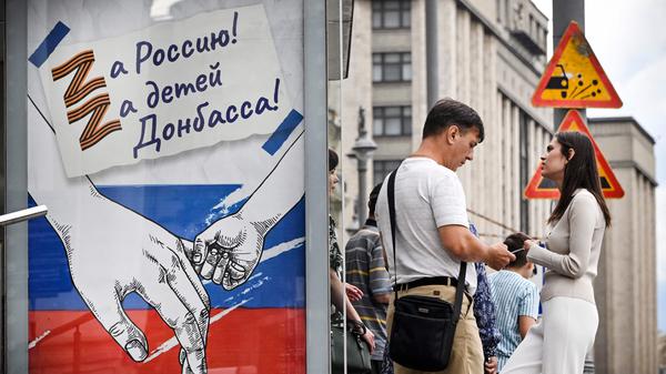 Menschen stehen in Moskau neben einem russischen Propagadaplakat. 