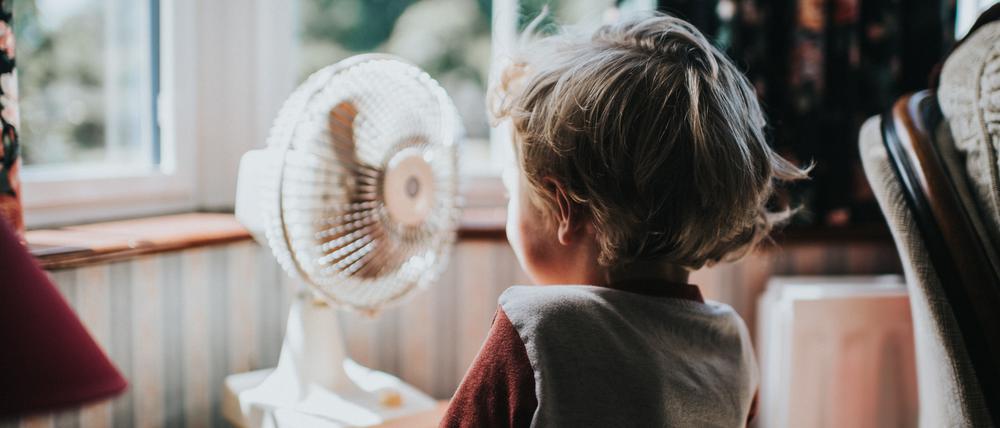 Ein kleiner Junge vor einem Ventilator. Es gibt noch andere Maßnahmen, um Räume kühl zu halten.