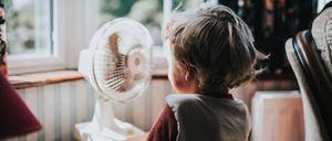 Ein kleiner Junge vor einem Ventilator. Es gibt noch andere Maßnahmen, um Räume kühl zu halten. 