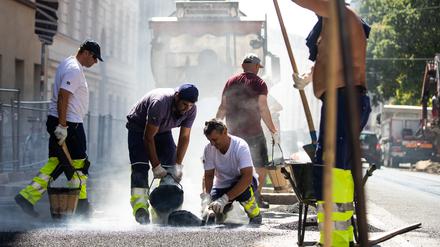 Straßenbauarbeitern macht zusätzlich zum glutgleichen Asphalt die pralle Sonne zu schaffen.