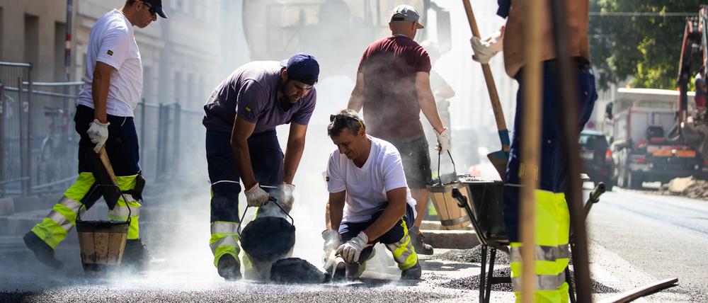 Straßenbauarbeitern macht zusätzlich zum glutgleichen Asphalt die pralle Sonne zu schaffen.