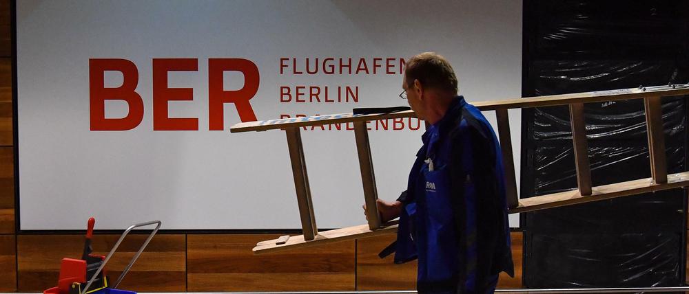 Installateur trägt Leiter vor einem BER-Schriftzug.