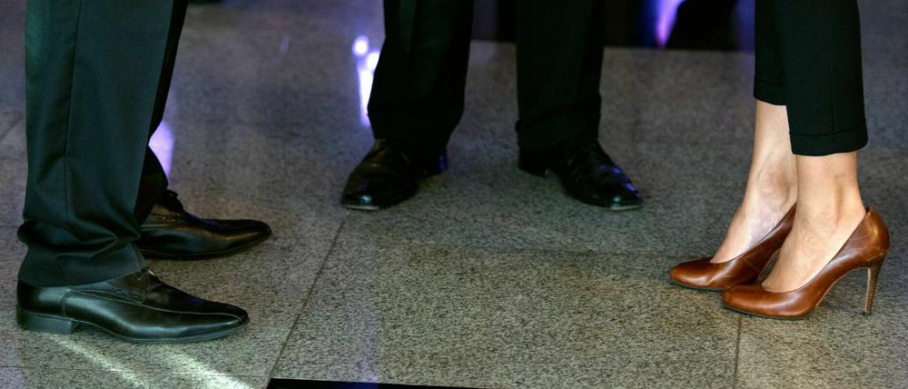 Die Beine und Füße von Männern in dunklen Anzügen und einer Frau mit hochhackigen Schuhen