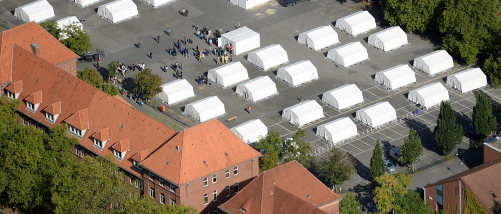 Flüchtlinge stehen am 09.09.2015 zwischen exakt ausgerichteten Zelten in der ehemaligen Schmidt-Knobelsdorf-Kaserne der Polizei in Berlin-Spandau vor einem Container der Senatsverwaltung. In den letzten Tagen sind hier über 300 Kriegsflüchtlinge angekommen, etwa 600 Flüchtlinge können untergebracht werden. Foto: Ralf Hirschberger/dpa ++ +++ dpa-Bildfunk +++