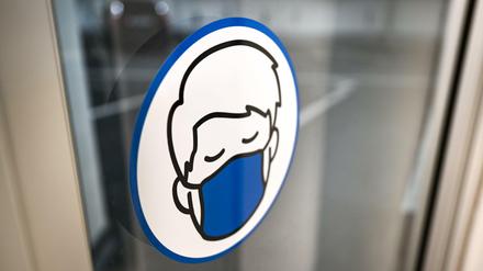 Ein Aufkleber, der auf die Maskenpflicht hinweist, ist in einem Parkhaus an der Türe angebracht.