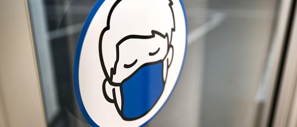 Ein Aufkleber, der auf die Maskenpflicht hinweist, ist in einem Parkhaus an der Türe angebracht.