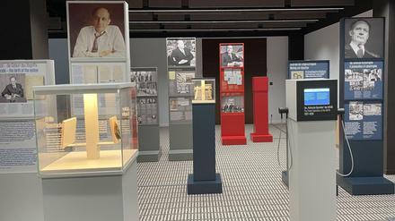 In einem Ausstellungsraum sind Stelen und Vitrinen mit Bildern und Texten zu sehen.