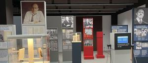 In einem Ausstellungsraum sind Stelen und Vitrinen mit Bildern und Texten zu sehen.
