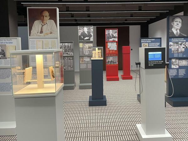 In einem Ausstellungsraum sind Stelen und Vitrinen mit Bildern und Texten zu sehen.
