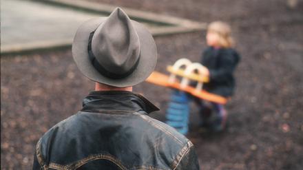 Ein Mann beobachtet ein spielendes Kind auf einem leeren Spielplatz (Symbolbild).