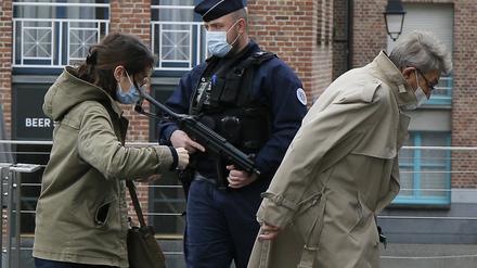 Passanten gehen an einem französischen Polizisten vorbei, der vor der Kirche Notre-Dame Wache steht. 