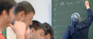 Eine junge Frau schreibt in einem Klassenraum etwas an die Tafel, junge Männer sitzen an Tischen und schreiben in ihre Hefte.