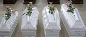 Särge, im Vordergrund vier Kindersärge mit Teddybären und Nummern