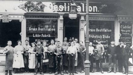 Schwarzweißaufnahme. 22 Mitarbeiter vor einem Ladengeschäft mit der Überschrift "Destillation"