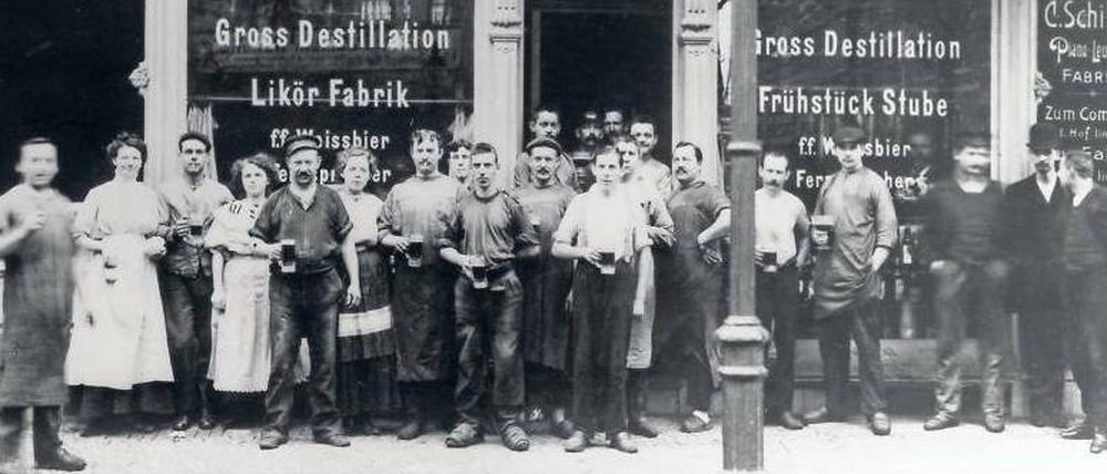 Schwarzweißaufnahme. 22 Mitarbeiter vor einem Ladengeschäft mit der Überschrift "Destillation"