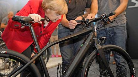 Angela Merkel beugt sich über ein schwarzes Fahrrad.