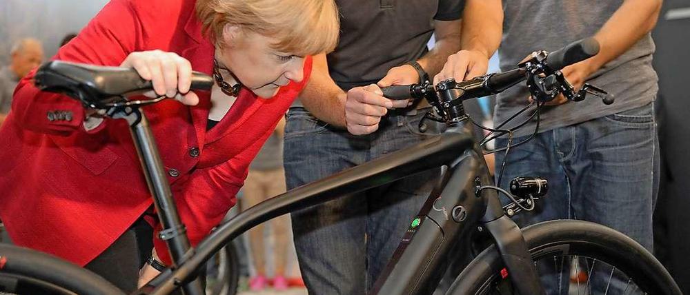 Angela Merkel beugt sich über ein schwarzes Fahrrad.