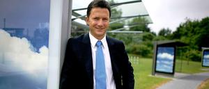 Udo Müller steht vor der Konzernzentrale des Unternehmens in Köln. Neben ihm ein Wartehäuschen mit einer Werbewand.