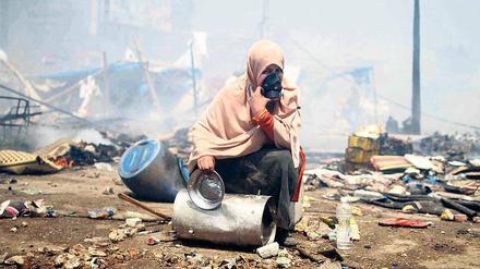 Vom Schutt umgeben. Eine Demonstrantin drückt sich im gestürmten Protestlager von Rabba al Adawiya in Kairo eine Atemmaske aufs Gesicht. Sicherheitskräfte hatten das Camp von Anhängern des entmachteten Präsidenten Mursi mithilfe von Tränengas geräumt. Foto: Mossab Elshamy/dpa