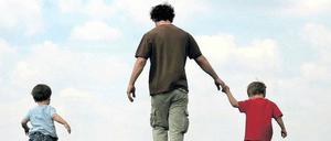 Ein Vater läuft mit seinen zwei kleinen Kindern über eine grüne Wiese.