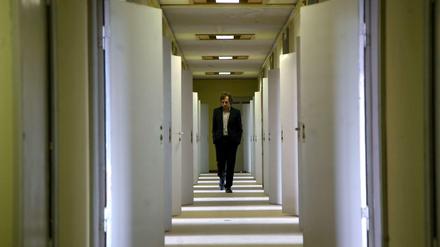 Ein Mann geht einen langen Gang im Stasi-Gefängnis in Hohenschönhausen entlang. Die Türen zu den Zellen sind geöffnet, Lichtstreifen fallen auf den Gang.