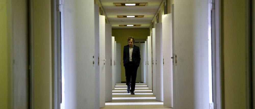 Ein Mann geht einen langen Gang im Stasi-Gefängnis in Hohenschönhausen entlang. Die Türen zu den Zellen sind geöffnet, Lichtstreifen fallen auf den Gang.