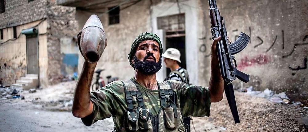 Ein Kämpfer der Freien Syrischen Armee hält seine Maschinenpistole und ein abgefeuertes Artilleriegeschoss der Regierungstruppen in den Händen.
