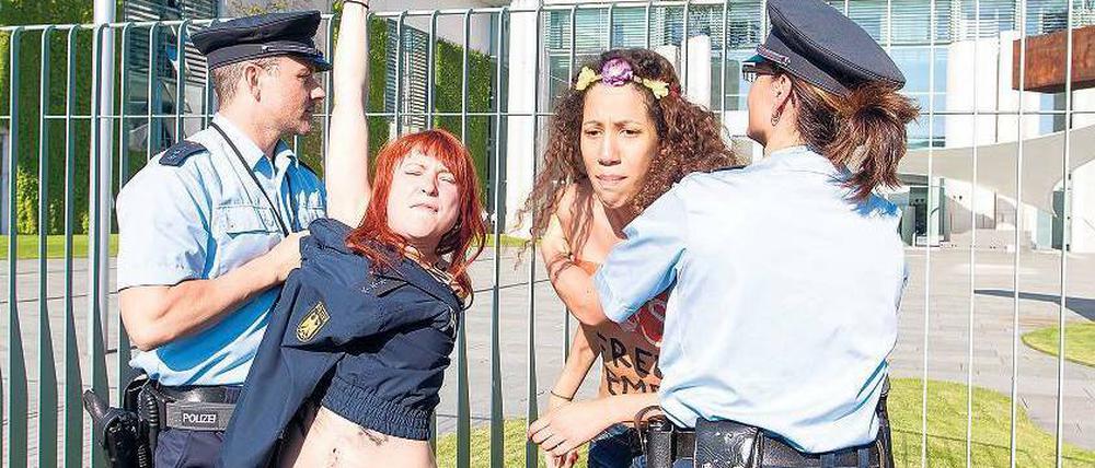 In Aktion. Polizisten bedecken vor dem Amtssitz der Kanzlerin die entblößten Oberkörper von zwei Femen-Aktivistinnen. Foto: Marcus Golejewski/Geisler-Fotopress