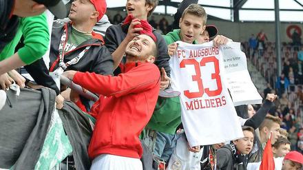 Zaunkönig Sascha Mölders grinst mit den Augsburger Fans um die Wette.