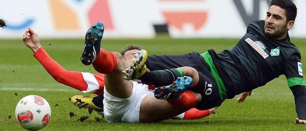 Bodenturnen: Der Mainzer Nikolce Noveski (l.) und der Bremer Mehmet Ekici landen beim Kampf um den Ball auf dem Rasen.