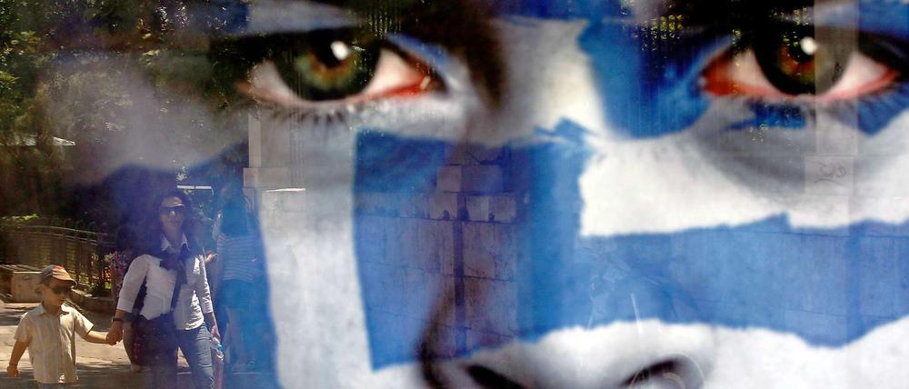 Passanten spiegeln sich in einem griechischen Wahlplakat.