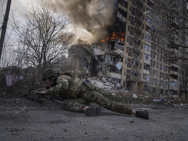 17.03.2023, Ukraine, Awdijiwka: Ein ukrainischer Polizist geht vor einem brennenden Gebäude in Deckung.